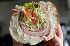 a hand holding a sandwich with meat, lettuce and tomatos on it