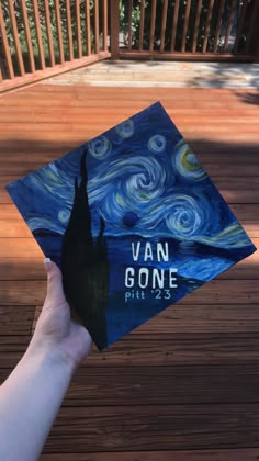 a hand holding up a blue graduation cap with the words van goghe written on it