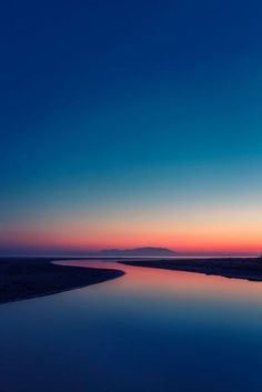 the sun is setting over a body of water with hills in the distance behind it