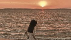 a woman standing on top of a sandy beach next to the ocean at sunset or dawn