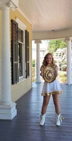 a woman in white and gold outfit holding a trophy on the front porch of a house