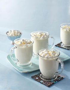 three mugs filled with hot chocolate and marshmallows on a blue table