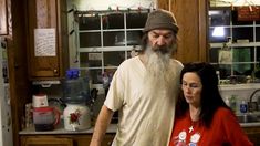 a man with a long white beard standing next to a woman in a red shirt