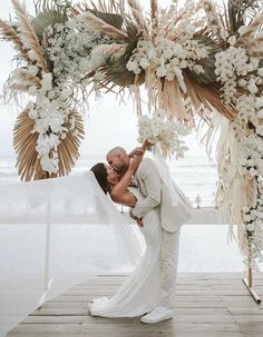 a bride and groom kissing under an outdoor wedding ceremony arch with flowers on the side