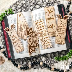 three wooden bookmarks with bats on them sitting on top of an open book next to beads