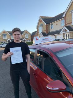 a man standing next to a red car holding up a certificate