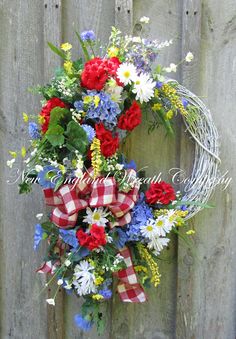 a wreath with red, white and blue flowers hanging on a wooden fence in front of it