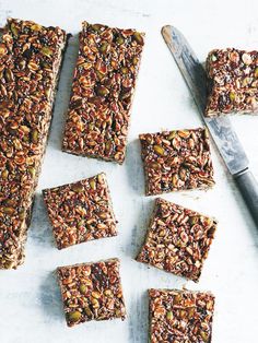 several squares of granola on a table next to a knife and cutting board with six bars