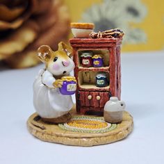 a small figurine of a mouse holding a cup in front of a cabinet