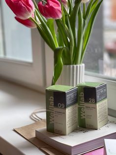 pink tulips in a white vase sitting on a window sill next to two boxes