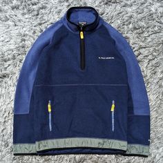 a blue jacket with yellow zippers sitting on top of a carpet