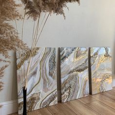 three paintings on the wall next to a vase with dry grass in it and some dried flowers