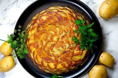 an apple pie on a black plate surrounded by lemons and parsley