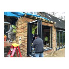 two men working on the side of a brick building with windows and roofing being installed