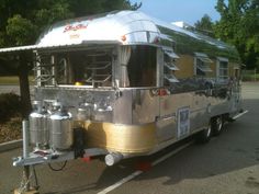 a silver trailer parked in a parking lot next to some trees and bushes on the side of the road