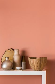 some vases and bowls are sitting on a white shelf against a pink painted wall