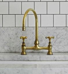 a kitchen sink with two brass faucets on the side and white subway walls