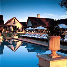 an outdoor swimming pool with chaise lounges and umbrellas in the evening light