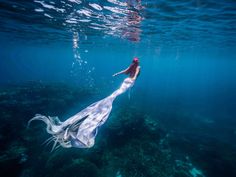 a woman is swimming in the ocean with her long white dress draped over her head