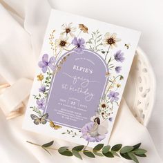 a purple and white floral birthday party card on a plate next to some green leaves