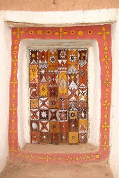 an artisticly designed window in the wall of a building that has been painted red, yellow and white