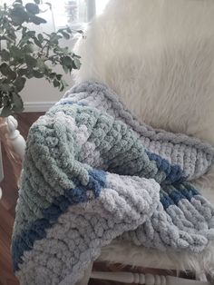 a white chair with a blue and gray blanket on top of it next to a potted plant