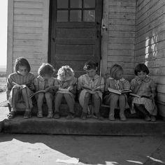 black and white photograph of children sitting on step reading books in front of building with door