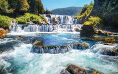 the water is flowing over rocks in front of a waterfall with trees on both sides