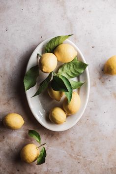 several lemons on a white plate with green leaves