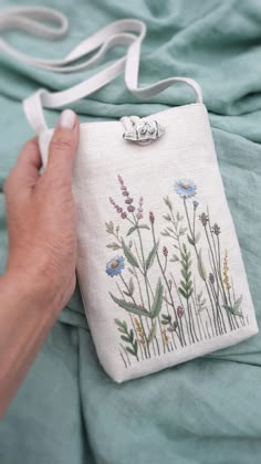 a hand holding an embroidered purse with flowers on it