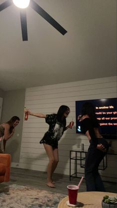 three women in a living room playing video games on the nintendo wii and drinking soda