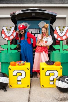 two people dressed up as mario and luigi in front of a trunk full of toys