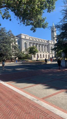 people are walking on the sidewalk in front of a large building with a clock tower