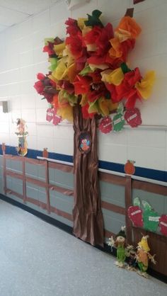 a classroom wall decorated with paper flowers and stuffed animals on the walls, in front of a tree