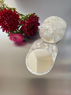 a white comb sitting on top of a table next to some red and pink flowers