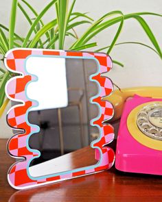 a pink phone sitting on top of a wooden table next to a mirror and potted plant