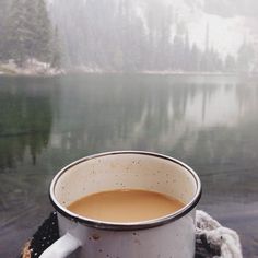 a cup of coffee sitting on top of a table next to a body of water