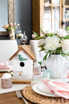 a table set with flowers, plates and napkins for a birdhouse centerpiece