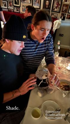 two people sitting at a table and one is holding a teddy bear in his hand