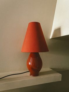 a red lamp sitting on top of a table next to a white wall and shelf