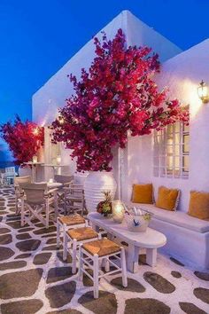 an outdoor patio with white furniture and flowers on the tree in front of it at night