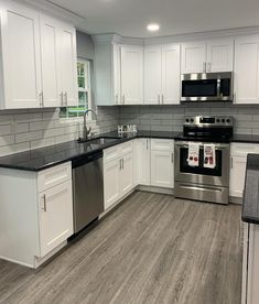 an empty kitchen with white cabinets and black counter tops, stainless steel appliances and wood flooring