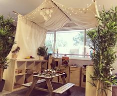 a room with some plants in it and a wooden table under the curtained window