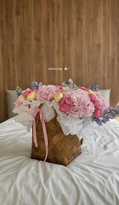 a basket filled with pink and white flowers on top of a bed next to a wooden headboard