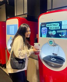 a woman standing in front of a machine holding a cup