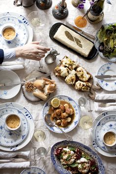 a table topped with plates and bowls filled with food next to wine glasses, silverware and utensils