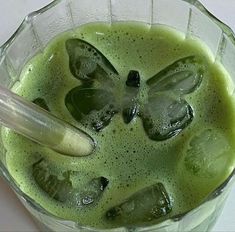 a pitcher filled with green liquid on top of a white table next to a spoon