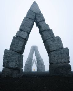 an arch made out of large rocks in the middle of a foggy field with a person standing between it