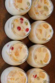 six glasses filled with liquid sitting on top of a wooden table