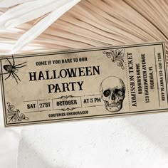 a ticket for a halloween party with a skull and spider web on the front is hanging from a ceiling